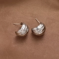 Dettaglio di orecchini a C in argento con texture martellata su tessuto di seta - Argento