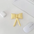 Close-up of a yellow checkered bow charm styled with a laptop and tech accessories - Yellow Plaid Bow Accessory