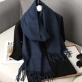 Detail view of a dark blue cashmere-feel scarf featuring soft fringe on a black coat - Navy Blue