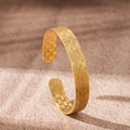 Detail of 18K gold-plated stainless steel cuff with intricate woven texture on sand - Houndstooth