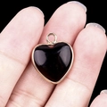 Golden heart-shaped pendant with black agate center held between fingers for size - Obsidian Gold Edging