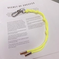 Détail d'un porte-clés en corde tressée jaune néon avec fermoir argenté sur un livre - 10.A05 Lanière Jaune Fluorescent