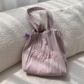 Detail of lavender striped canvas tote bag with pink Bonjour embroidery on soft sofa - Pink