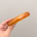 Close-up of a thick translucent orange agate resin bangle held by a hand on grey background - Amber