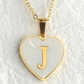 Golden heart necklace with pearl inlay and letter J pendant on a white fabric surface - Letter J / Gold