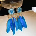 Détail de boucles d'oreilles bohèmes à plumes bleues sur un support en verre - Crochets d'oreilles ronds à plumes bleues