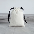 Detail of white cotton jewelry pouch with black ribbon drawstring on gray fabric - 7x9cm