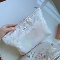 Dettaglio della borsa da trucco in raso rosa con motivi floreali e cerniera - Rosa