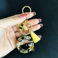 Close-up of resin letter G keychain with dried daisy, gold foil, and a bee charm - Letter G
