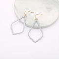 Detailed macro view of light blue hollowed-out teardrop earrings on marble tray - Light Gray
