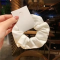 Minimalist white ribbed fabric scrunchie shown in hand with a soft indoor cafe background - Artistic Girl Soft White