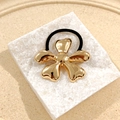 Golden flower metallic hair tie with black elastic band on white marble texture base - Flower Hair Tie