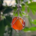 Close-up of raw orange crystal pendant in silver metal cage on a natural green background - Red Agate