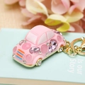 Pink car keychain with sparkling rhinestones and gold clasp shown against soft flowers - Beetle Car Pink