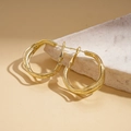 Dettaglio di orecchini a cerchio triplo dorati con linee ondulate organiche materiche - Oro