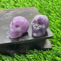 Pair of carved amethyst crystal skulls on wooden base set against a green lawn - Phosphosiderite