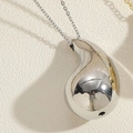 Detalle de un colgante de gota de plata con superficie pulida sobre fondo texturizado - Gota de Agua Oro Blanco / Plateado