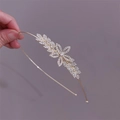 Detail of a gold floral rhinestone headband with pearl accents held by hand on grey background - Leaf