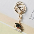 Golden graduation keychain with black mortarboard and graduate scroll on book page - Style 2 (Lobster Clasp)