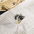 Detail van verstelbare drakenvleugel ring met zwarte glitters op vintage papier decor - Grijs