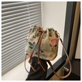 Detail of floral embroidery on beige fabric bucket bag with brown drawstring and gold hardware - Style 2
