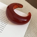 Detail of amber resin cuff bracelet with polished finish on a minimalist book background - Caramel Red (Red-Round Open)
