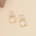 Detail of gold-plated drop earrings featuring two rectangular clear crystals on beige back - White