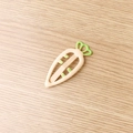 Beige carrot-shaped hair clip with green leaves on a wooden texture background - Ivory