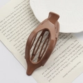 Glossy brown oval duckbill hair clip placed on a book page for elegant styling - Bright Coffee