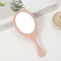 Pink handheld makeup mirror with vintage embossed frame on a decorative background - Pink