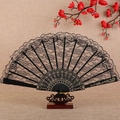 Elegant black lace folding fan with floral patterns and gold detailing on a wooden stand - Black