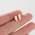 Macro shot of rose gold leaf stud earrings with a polished finish held on fingertips - Leaf / Rose Gold