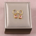 Detalle de pendientes dorados con gemas rosas rectangulares sobre joyero color beige - 26b06021-pink diamond earrings