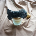 Close-up of black woven leather bow hair clip on a vintage decorative candle jar - Black Bow