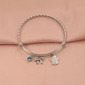 Brazalete de plata con piedra azul, lazo y dije de ángel sobre fondo de satén rosa - Color Acero