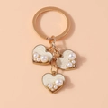 Dettaglio di ciondoli a cuore dorati con smalto bianco e perle su un portachiavi raffinato - Bianco