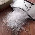 Dettaglio degli elastici per capelli trasparenti in un sacchetto a chiusura con pinguino - Circa 1000 Pezzi/Sacco / Trasparente
