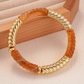 Dettaglio ravvicinato di segmenti in metallo dorato e resina ambrata su bracciale elastico - Caffè Chiaro