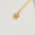 Collana a stella solare placcata oro con zirconi lucidi su sfondo in pietra chiara - Piccolo sole / Oro 14K