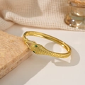 Goldenes Schlangenarmband mit grünen Steinaugen und weißen Zirkonia auf Steinuntergrund - Gold