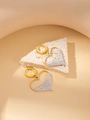 Goldene Herzohrringe mit weißen Zirkonia-Steinen auf einem hellen Steinsockel - Meer der Liebe Ohrringe mit weißem Zirkon