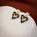 Detalle macro de pendientes de corazón en cuero trenzado y perlas sobre cerámica blanca - Estilo Perla de Corazón de Cadena Tejida en Oro Negro