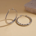 Détail de créoles argentées avec texture martelée sur fond de pierre naturelle sobre - Boucle d'Oreille Moyenne / Argenté