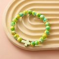 Detail of yellow and green beaded bracelet with a light green cross charm on a tray - Yellow Green Spotted Light Green Cross Bracelet