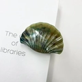 Green marble textured shell-shaped hair claw clip in acetate finish on book background - Jade Olive Brown