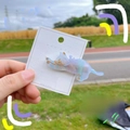 Detailed close-up of a dreamy blue cat hair clip on a branded UYU card against nature - Clear Blue