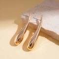Macro shot of polished gold water drop earrings on a light textured stone base - Gold
