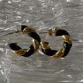 Macro view of twisted black and gold C-shaped earrings on a water ripple glass surface - Black/Gold