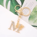 Golden metal butterfly and crystal letter M keychain on elegant white artistic background - Letter M