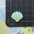 Macro detail of a 2cm green and white resin seashell charm on a measurement scale mat - Green and White Shell